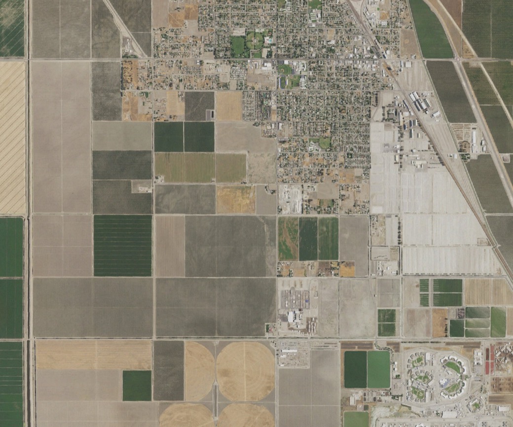 Straight-down aerial of a Central Valley town and its surrounding farm grid, with a site boundary drawn over it